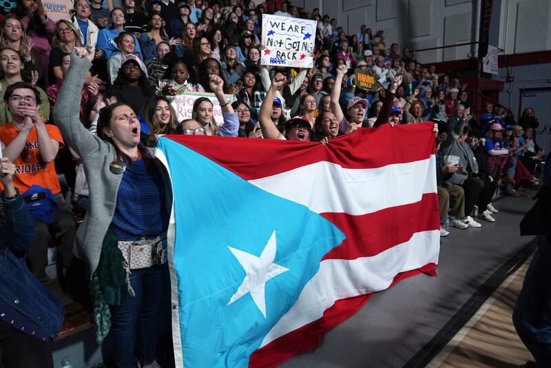 Asistentes sostienen la bandera de Puerto Rico mientras el alcalde de Allentown, Pensilvania, Matt Tuerk, habla durante un acto de campaña de la candidata presidencial demócrata a la vicepresidenta Kamala Harris en el Memorial Hall del Muhlenberg College en Allentown, Pensilvania, el lunes 4 de noviembre de 2024. (Foto AP/Susan Walsh)