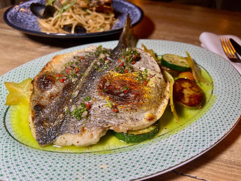 Branzino, un pescado entero asado, servido con aceite de limón y papas perla con vegetales.