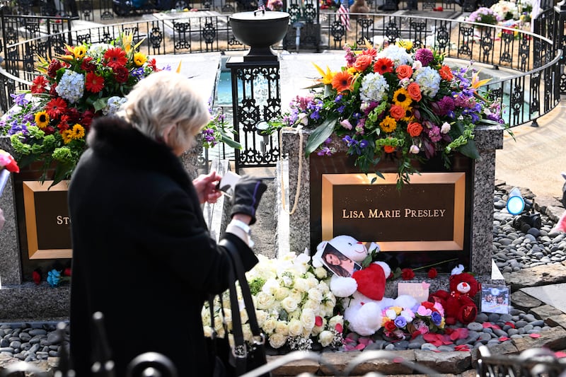 A visitor stops to take a photo of the gravesite after a memorial service for Lisa Marie Presley Sunday, Jan. 22, 2023, in Memphis, Tenn. She died Jan. 12 after being hospitalized for a medical emergency and was buried on the property next to her son Benjamin Keough, and near her father Elvis Presley and his two parents. (AP Photo/John Amis)