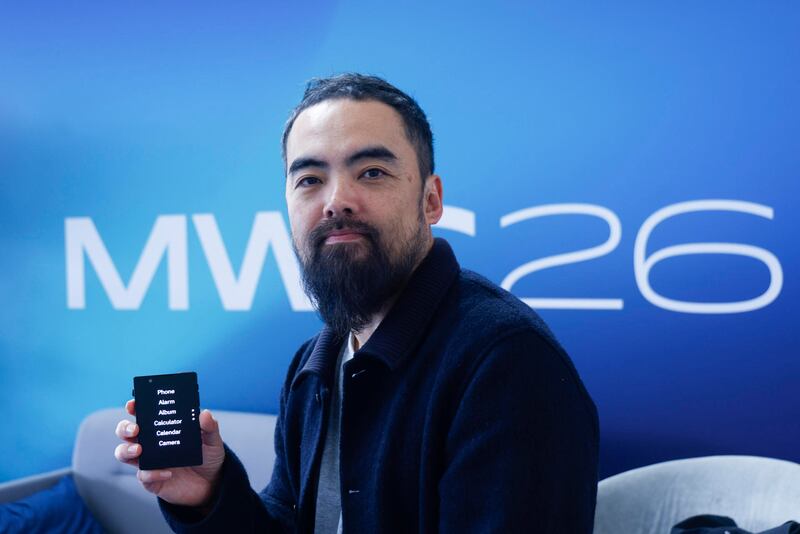 El consejero delegado de Light Phone, Kaiwei Tang, posa con uno de los móviles de su compañía, aparatos minimalistas diseñados para reducir la adicción a las pantallas y mejorar el bienestar digital, especialmente entre los jóvenes, en el marco del MWC 2026. EFE/ Quique García
