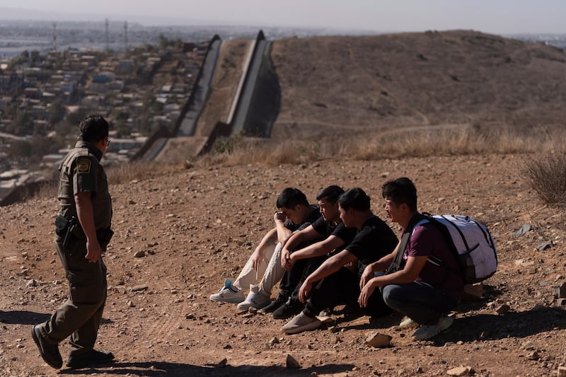 Un agente de la Patrulla Fronteriza pasa junto a cuatro hombres detenidos después de cruzar ilegalmente la frontera México-EEUU, en San Diego. (AP Foto/Gregory Bull)
