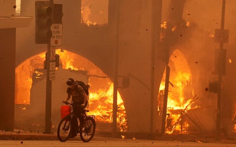 Un ciclista pasa frente a una estructura en llamas en Lake Avenue, en la sección de Altadena en Pasadena, Calif. (AP Photo/Chris Pizzello)
