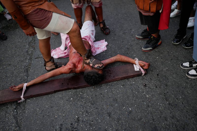 Un devoto caracterizado de soldado romano coloca su pie sobre la cara de un penitente que interpreta a uno de los dos ladrones condenados a la crucifixión junto a Jesucristo, durante una recreación del Vía Crucis como parte de la celebración de la Semana Santa, en el vecindario de Petare de Caracas, Venezuela, el 29 de marzo de 2024. La Semana Santa conmemora los últimos días de la vida de Jesús, según la Biblia, incluyendo su crucifixión el Viernes Santo y su resurrección en el Domingo de Pascua. (AP Foto/Matías Delacroix)