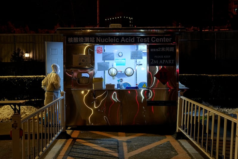 Un sanitario entra en una cabina de pruebas de detección del COVID-19 tras desinfectar el cristal en el estacionamiento del hotel Shangri-La, durante los Juegos Olímpicos de Invierno, el 16 de febrero de 2022, en Beijing. (AP Foto/Jae C. Hong)