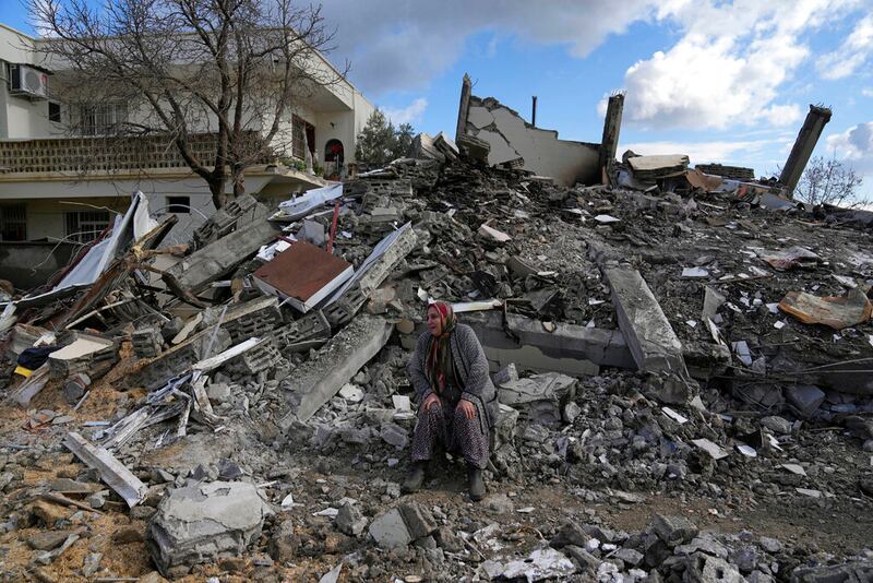 Una mujer está sentada sobre los escombros mientras los equipos de rescate buscan gente debajo de los restos de edificios en la población de Nurdagi, en el sur de Turquía, martes 7 de febrero de 2023. El poderoso terremoto que remeció Turquía y Siria el lunes ha dejado un saldo de más de 5.000 muertos, cifra que se prevé aumentará.