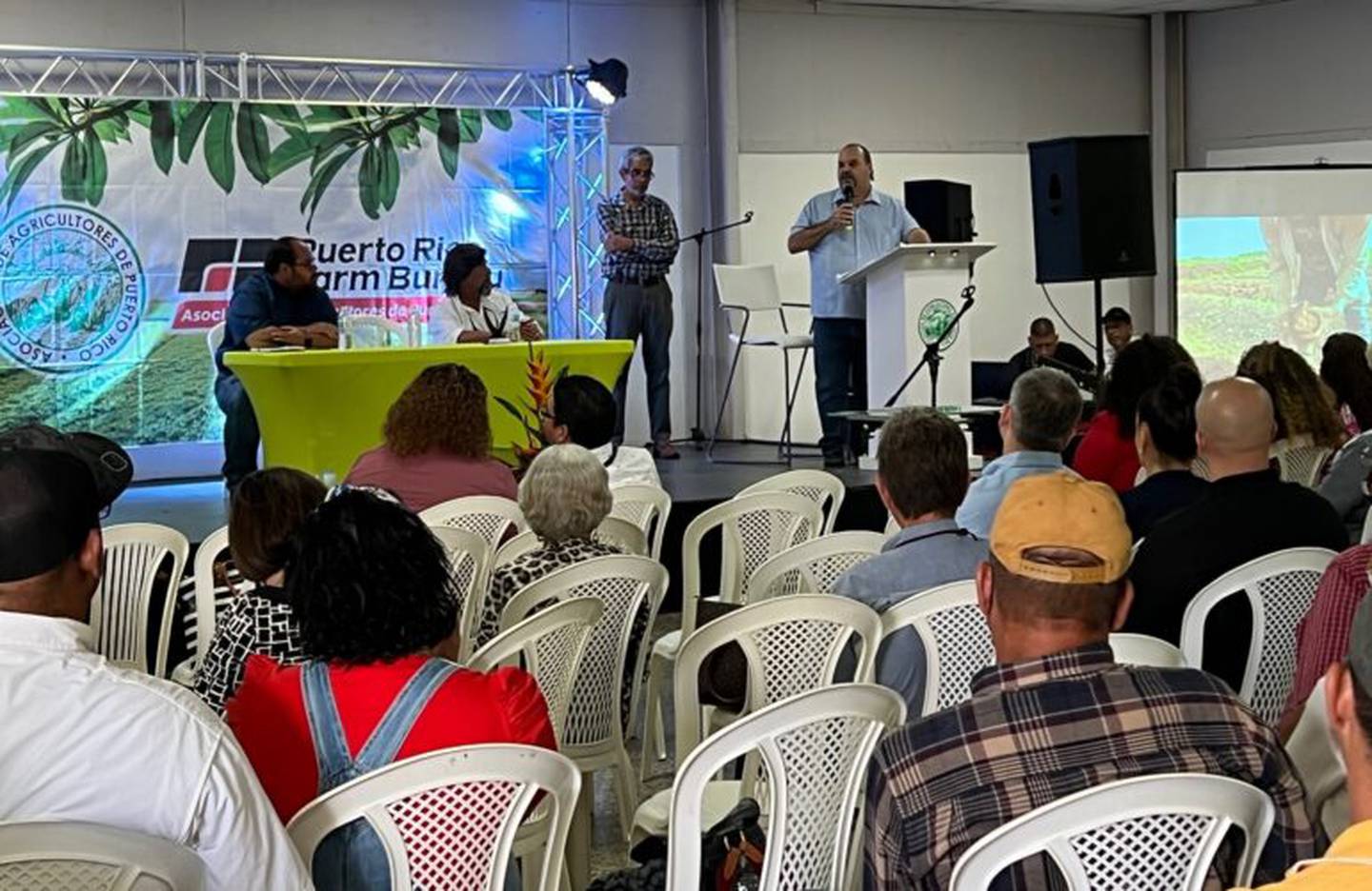 El secretario del Departamento de Agricultura se dirige a los agricultores durante la asamblea anual de la Asociación de Agricultores de Puerto Rico. Detrás y de pie, Héctor I. Cordero Toledo, presidente de la asociación.