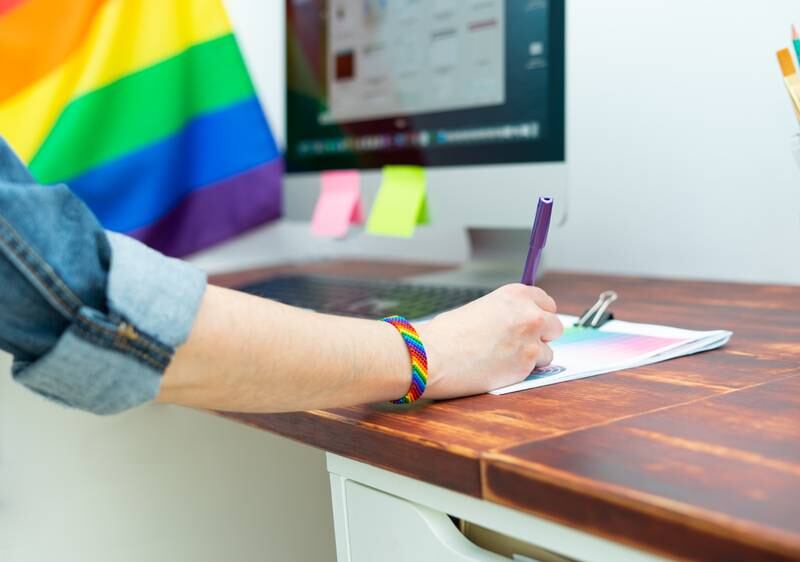 Persona escribiendo encima de un escritorio con decoraciones LGBTQIA+.