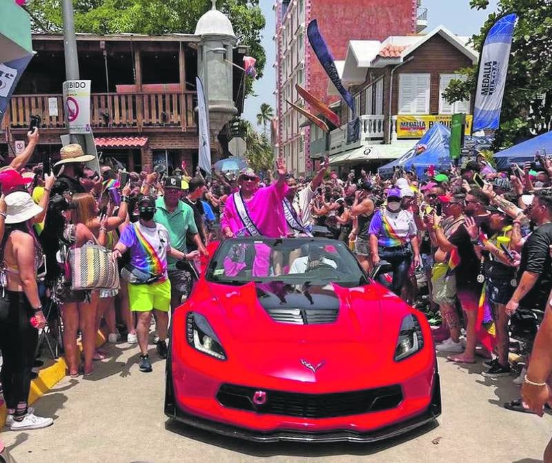 Vehículo de lujo rodeado de personas celebrando la llegada del mes de junio, mes LGBTQIA+.