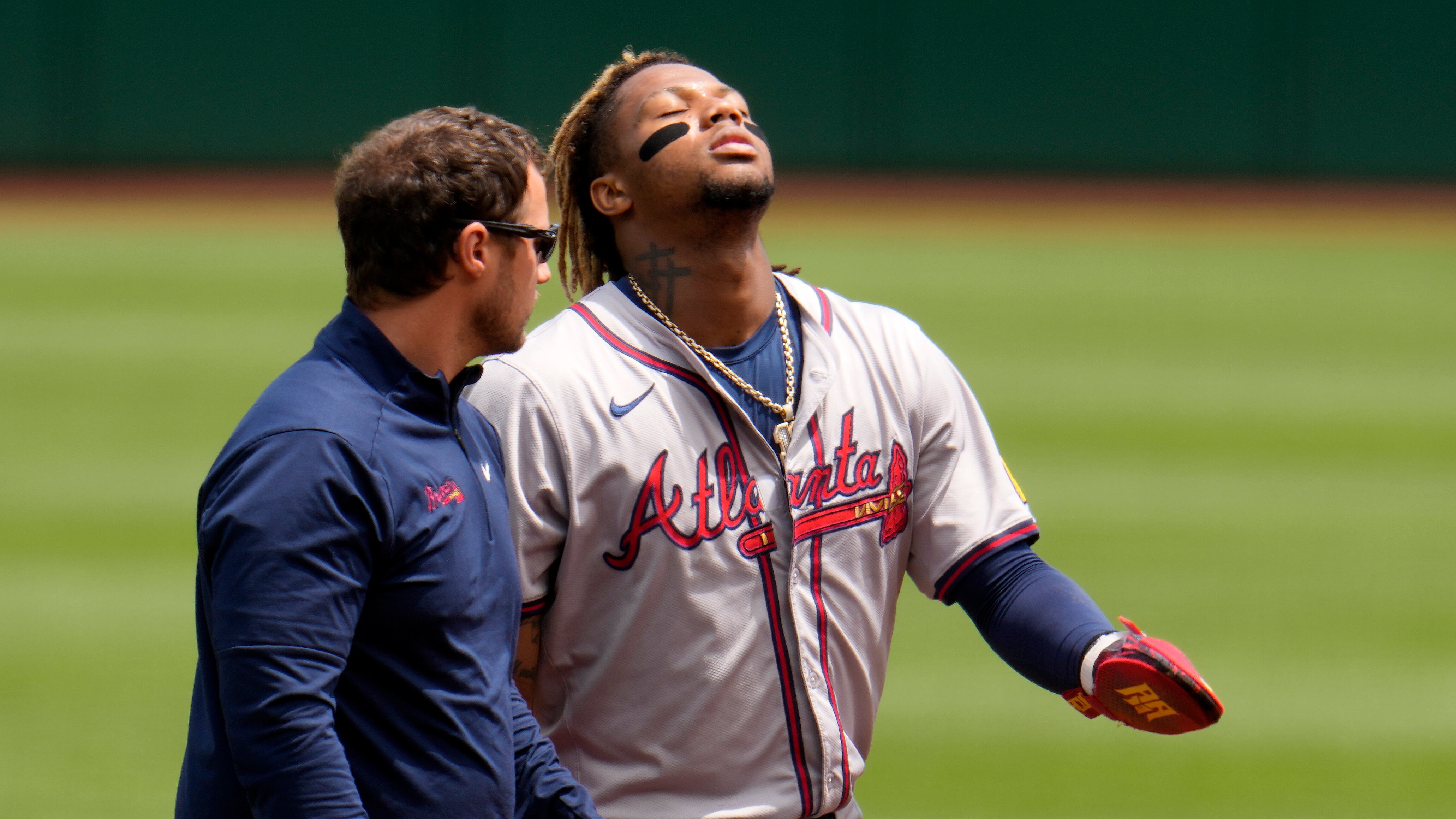 Ronald Acuña Jr., derecha, de los Bravos de Atlanta, camina para abandonar el campo acompañado del asistente médico después de sufrir una lesión al intentar robarse tercera durante la primera entrada del juego de béisbol en contra de los Piratas de Pittsburgh, el domingo 26 de mayo de 2024, en Pittsburgh. (AP Foto/Gene J. Puskar)