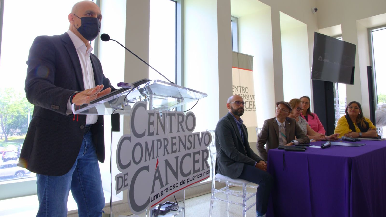Periodista Alex Delgado en un atril en el evento del Centro Comprensivo de Cáncer.