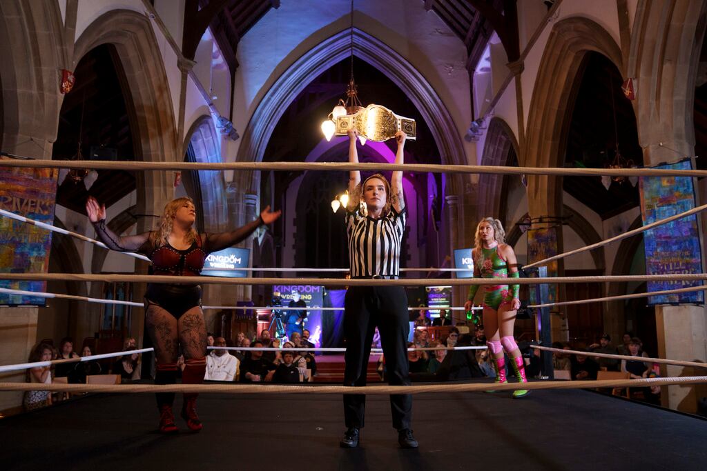 La árbitro Katie Crosby sostiene el cinturón en disputa antes del combate de Kiara contra Scarlett, izquierda, durante un espectáculo de Kingdom Wrestling, el sábado 29 de marzo de 2025, en la iglesia de San Pedro, Shipley, Reino Unido. (AP Foto/Jon Super)