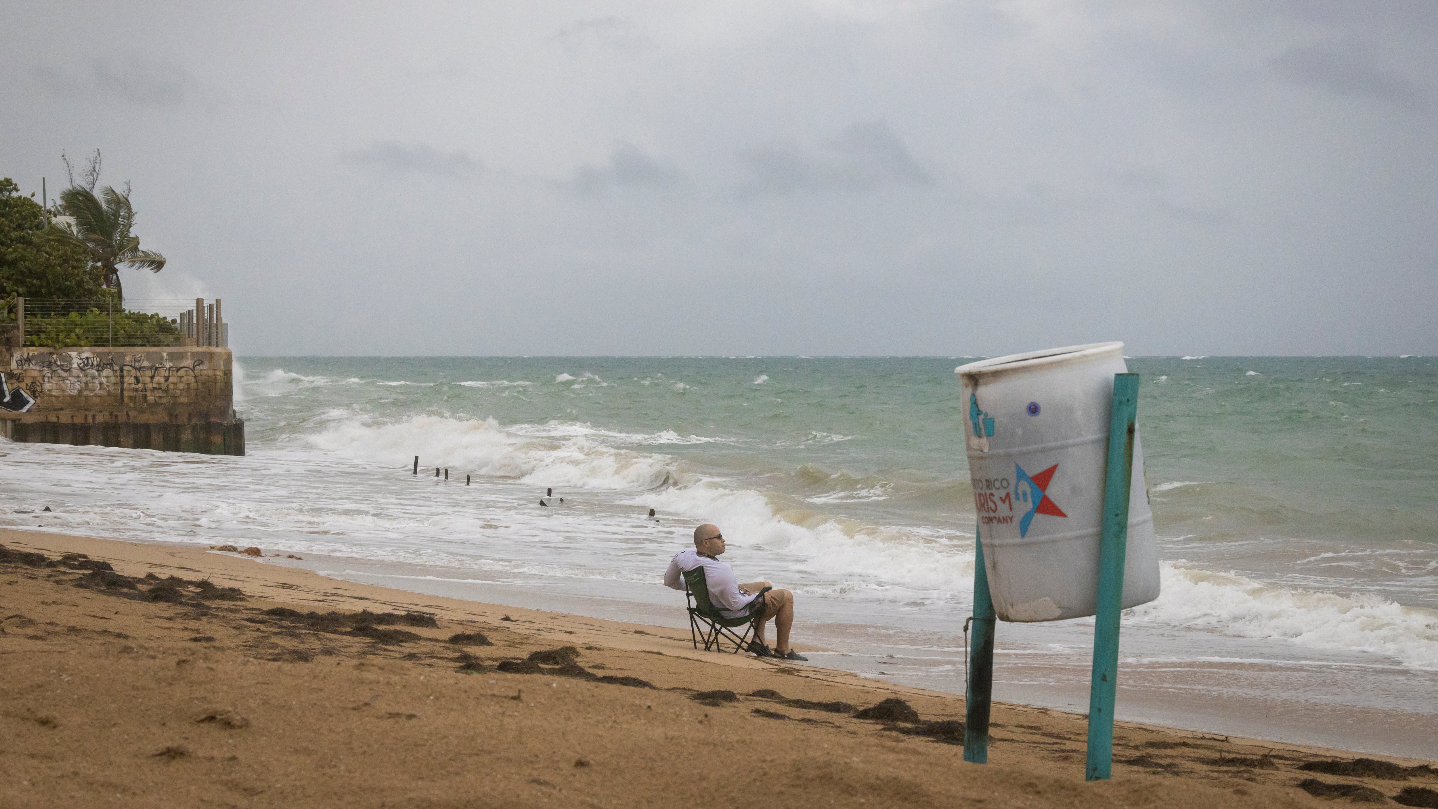 Un hombre se sienta en la playa mientras rompen las olas, antes de la llegada de la tormenta tropical Fiona en San Juan, Puerto Rico, el sábado 17 de septiembre de 2022.