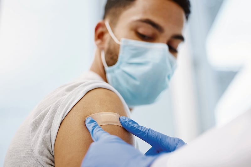Le colocan una curita a un joven en el brazo después de ponerle una vacuna.