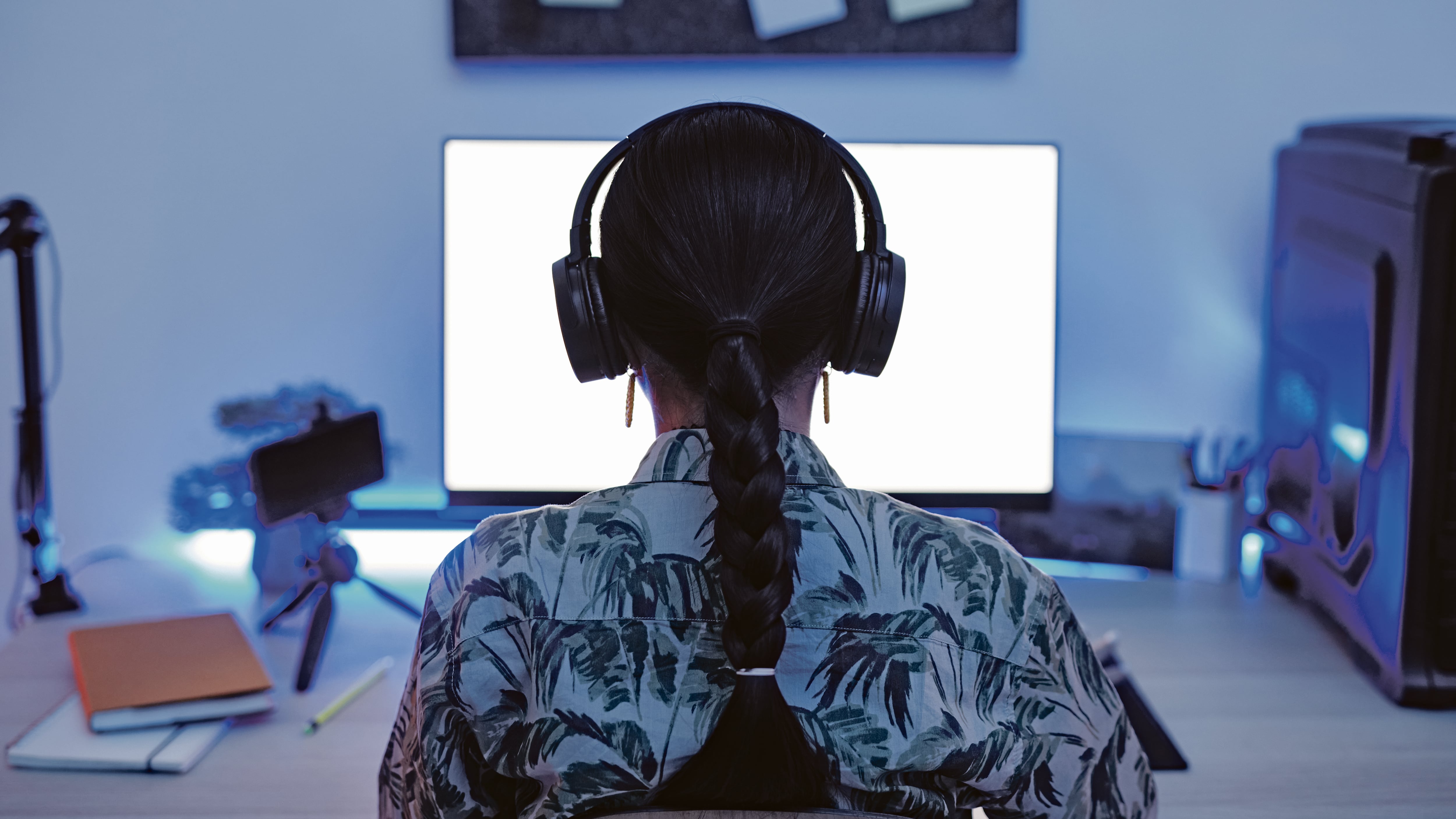 Chica con auriculares frente a un ordernador, sentada en su escritorio.