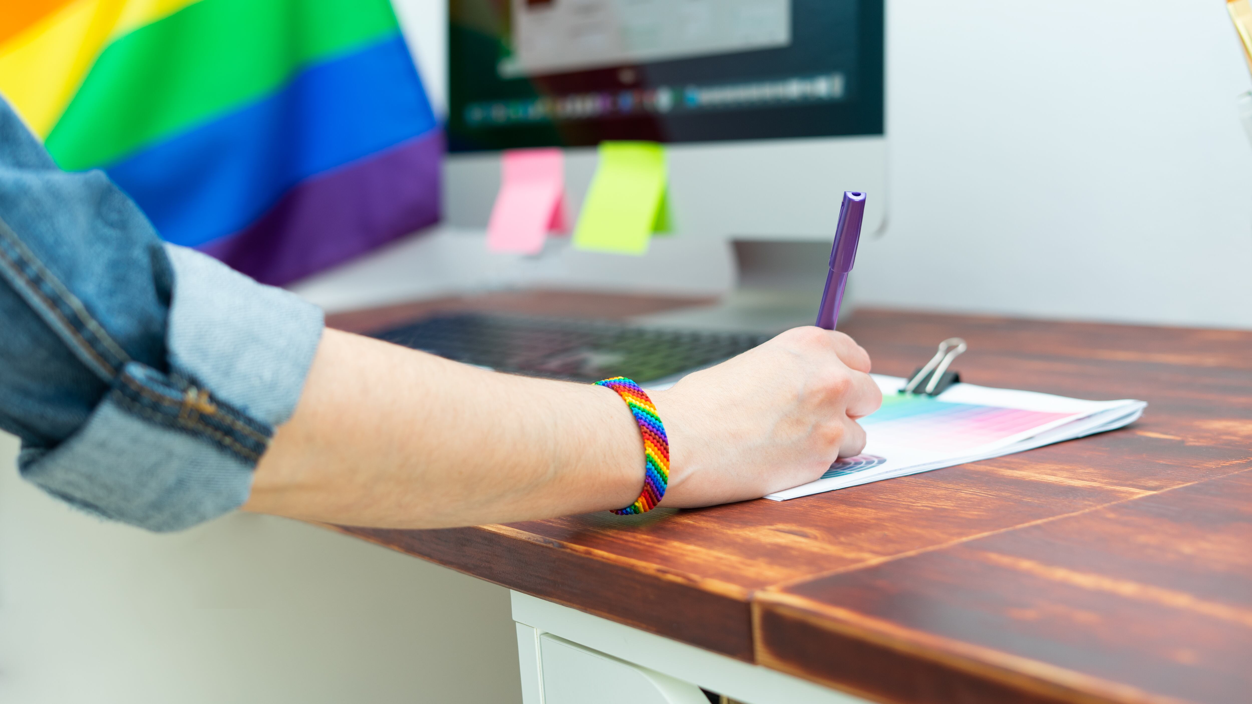 Persona escribiendo encima de un escritorio con decoraciones LGBTQIA+.