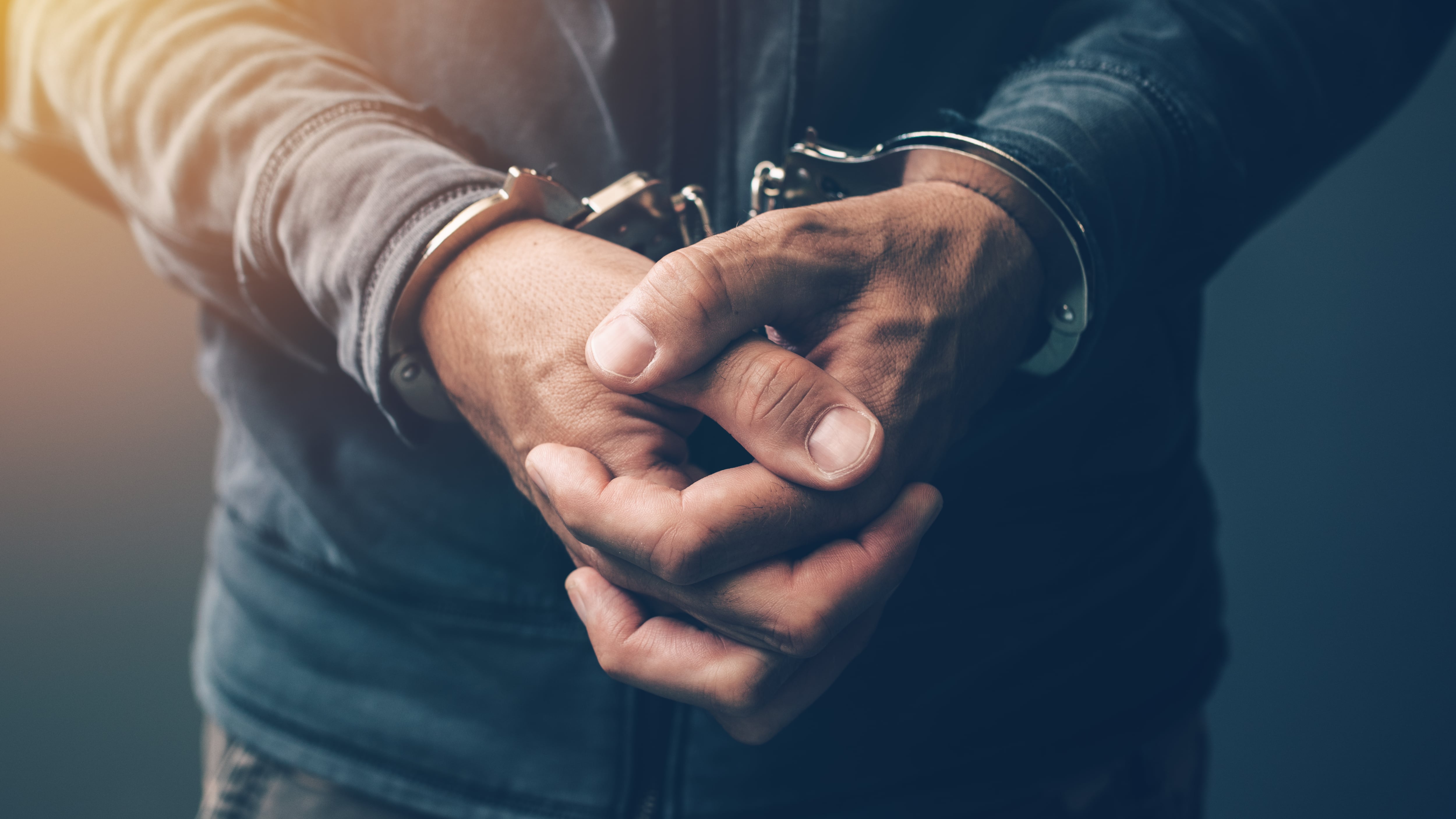 Delincuente arrestado con esposas, primer plano de las manos.