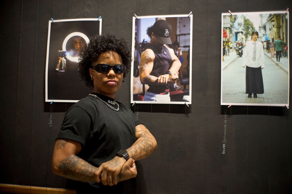 Davon Cornell Suárez, un hombre transgénero, posa frente a la impresión de su retrato realizada por el fotógrafo transgénero Merle Ramírez en la exposición de Ramírez sobre la comunidad transgénero en la galería La Marca en La Habana, el viernes 4 de abril de 2025. (AP Foto/Ramón Espinosa)