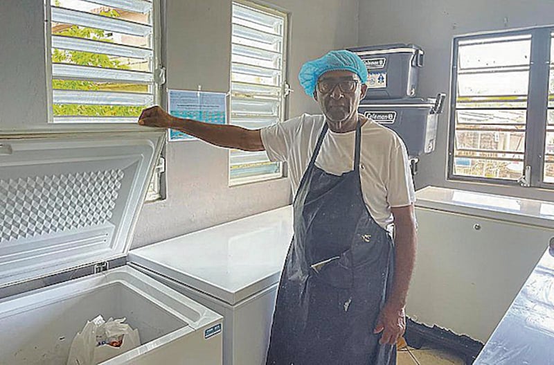 Wilson Vellón sostiene con su mano derecha la puerta o tapa de uno de sus congeladores, prácticamente vacío. Lleva puesto un delantal y una redecilla en su cabeza.