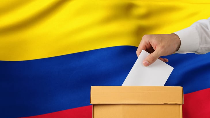 Election in Colombia. Man hand putting his vote into ballot box and Colombia flag on background - Close up