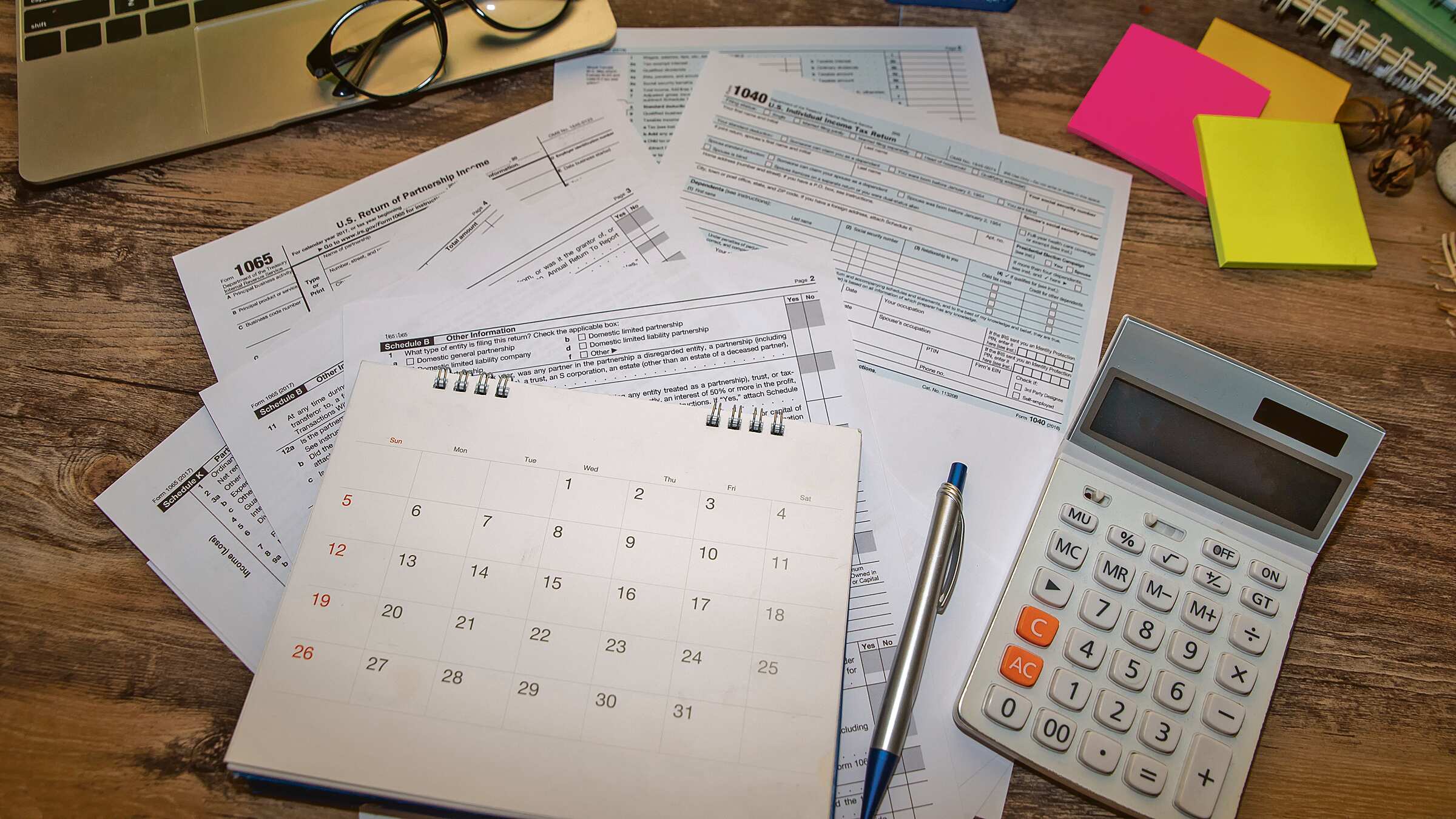 Papeles, un calendario y una calculadora sobre una mesa, reflejando la situación de una persona que está llenando sus planillas.