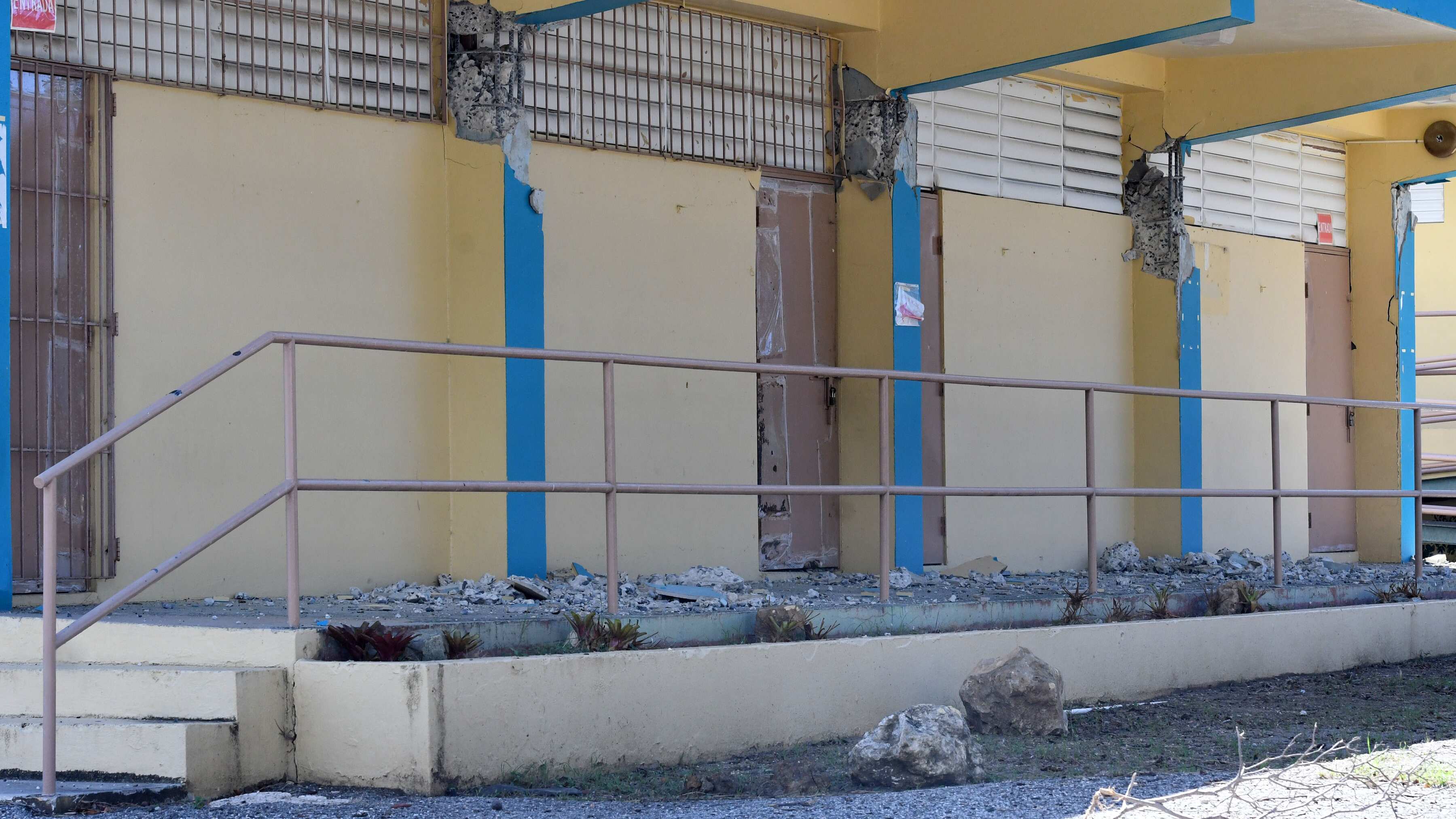 Un edificio escolar con las columnas destrozadas. Se ven los alambres y el concreto al descubierto, mientras que el piso, un pasillo, está repleto de pedazos de la estructura.