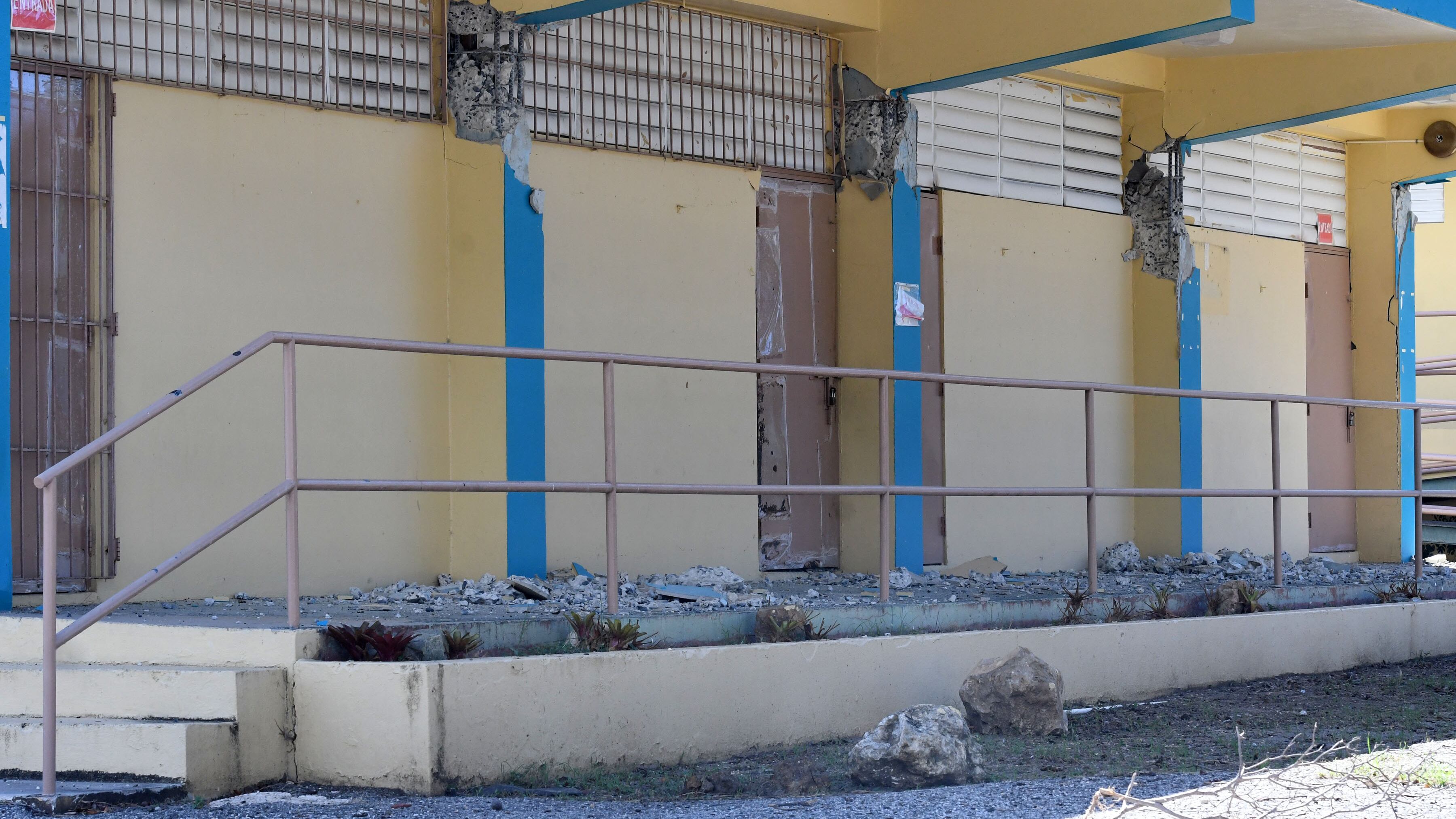Un edificio escolar con las columnas destrozadas. Se ven los alambres y el concreto al descubierto, mientras que el piso, un pasillo, está repleto de pedazos de la estructura.