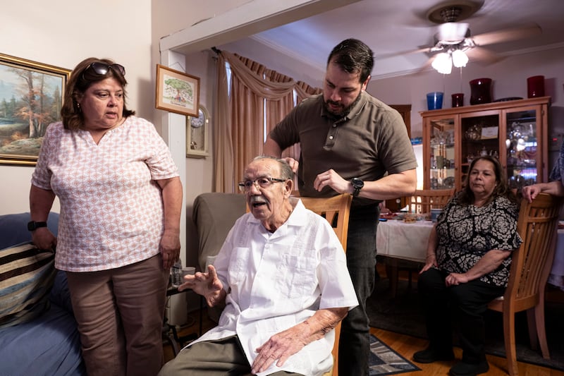 Adrián Valderrama, 50, le peina el cabello a su padre, Fernando, 93, junto a sus hermanas Noemí, 65, izquierda, y Nilda, 69, a la derecha, en el comedor de la residencia familiar. Chicago, Illinois, 1 de septiembre de 2025. Los siete  hermanos Valderrama se dividen el tiempo para el cuidado de Fernando, quien reside en San Sebastian, Puerto Rico por seis meses al año. (foto/Herminio Rodriguez©)