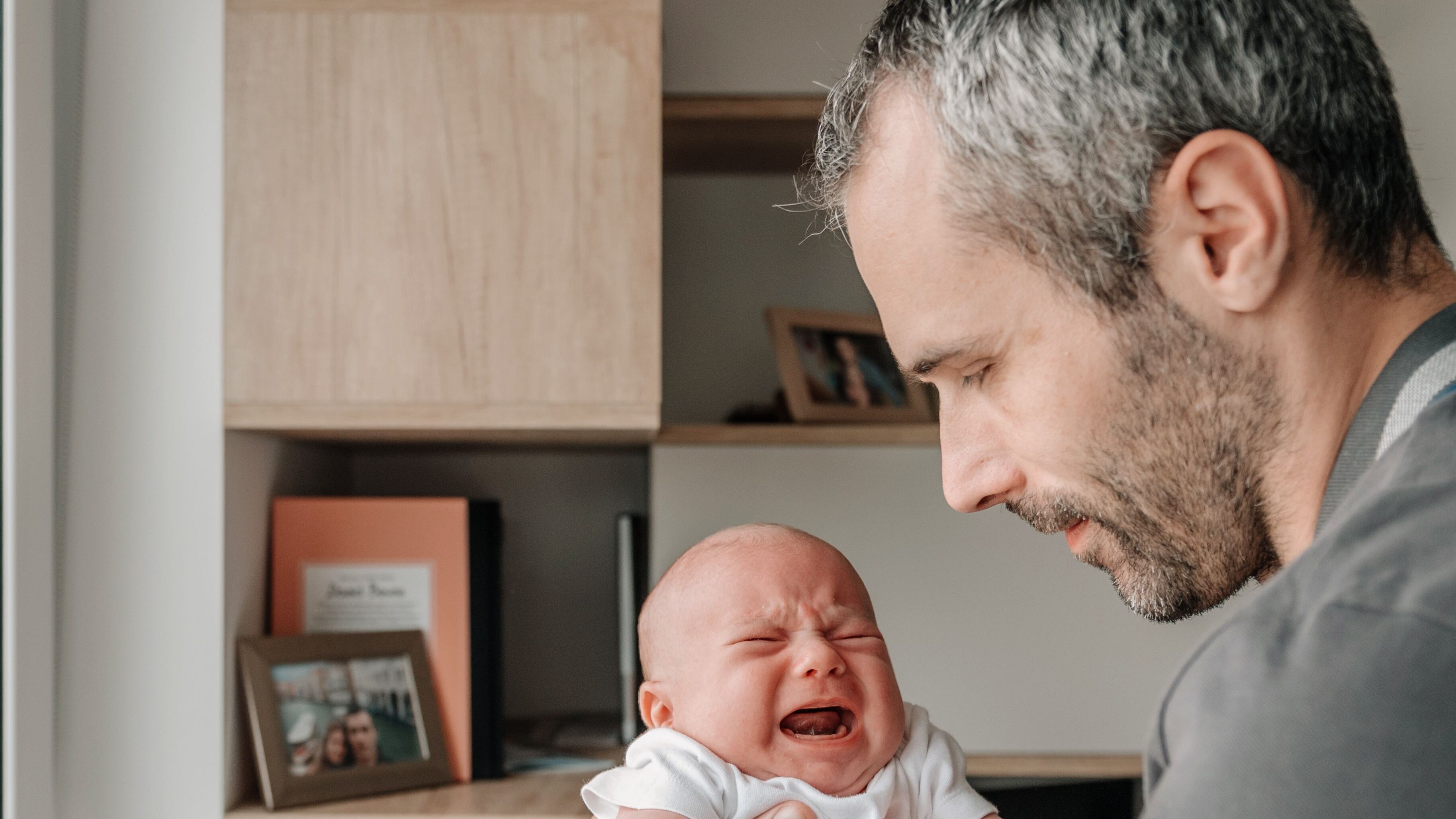 Padre blanco aguantando a su bebe mientras llora.