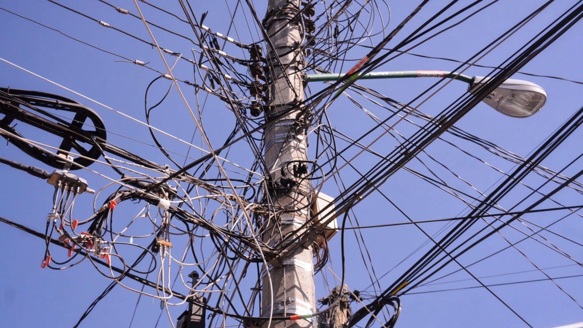 Vista de un poste de luz lleno de cables de telecomunicaciones.