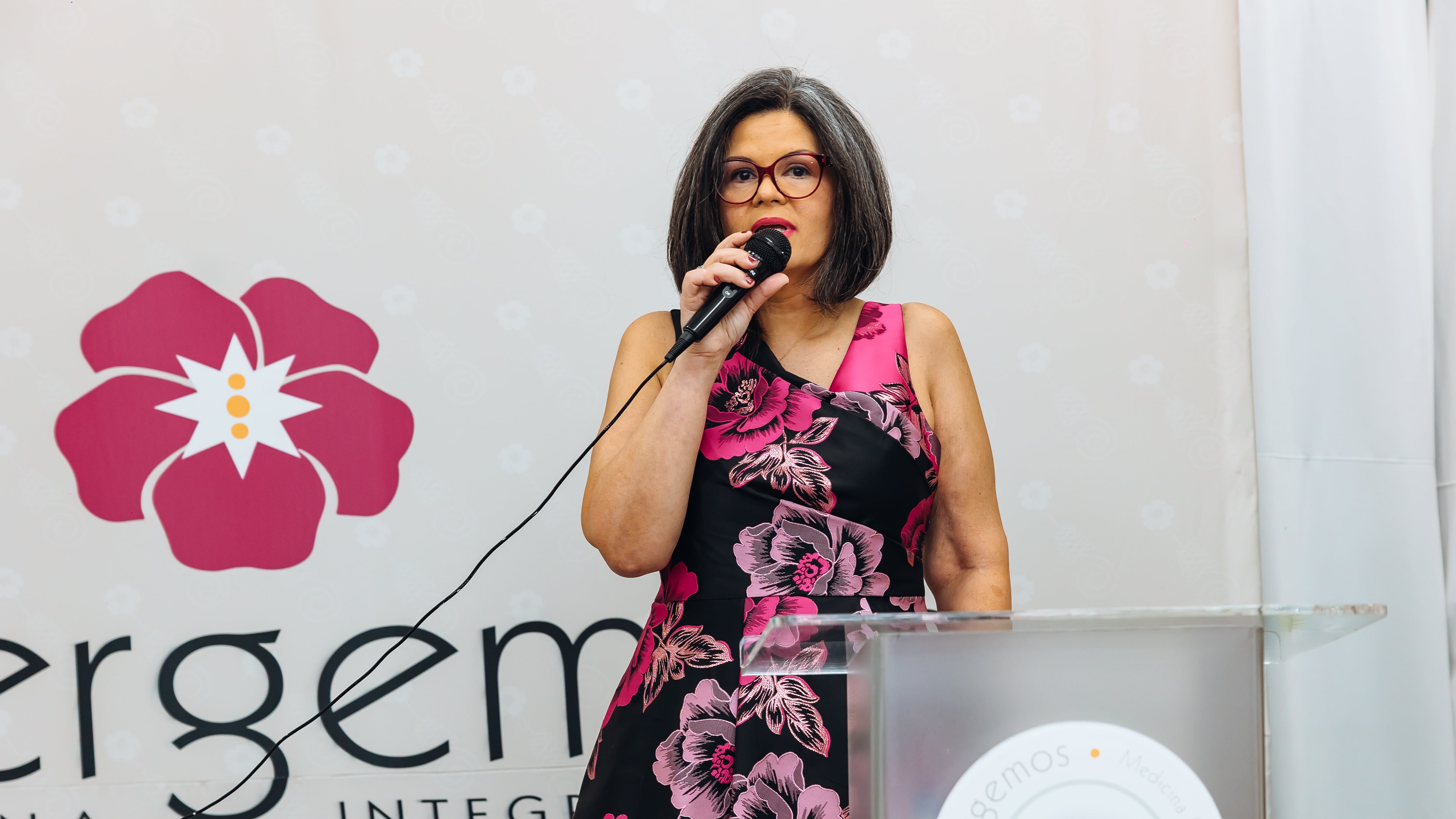Doctora Maribel Campos sujeta micrófono frente a fondo con logo de Emergemos.