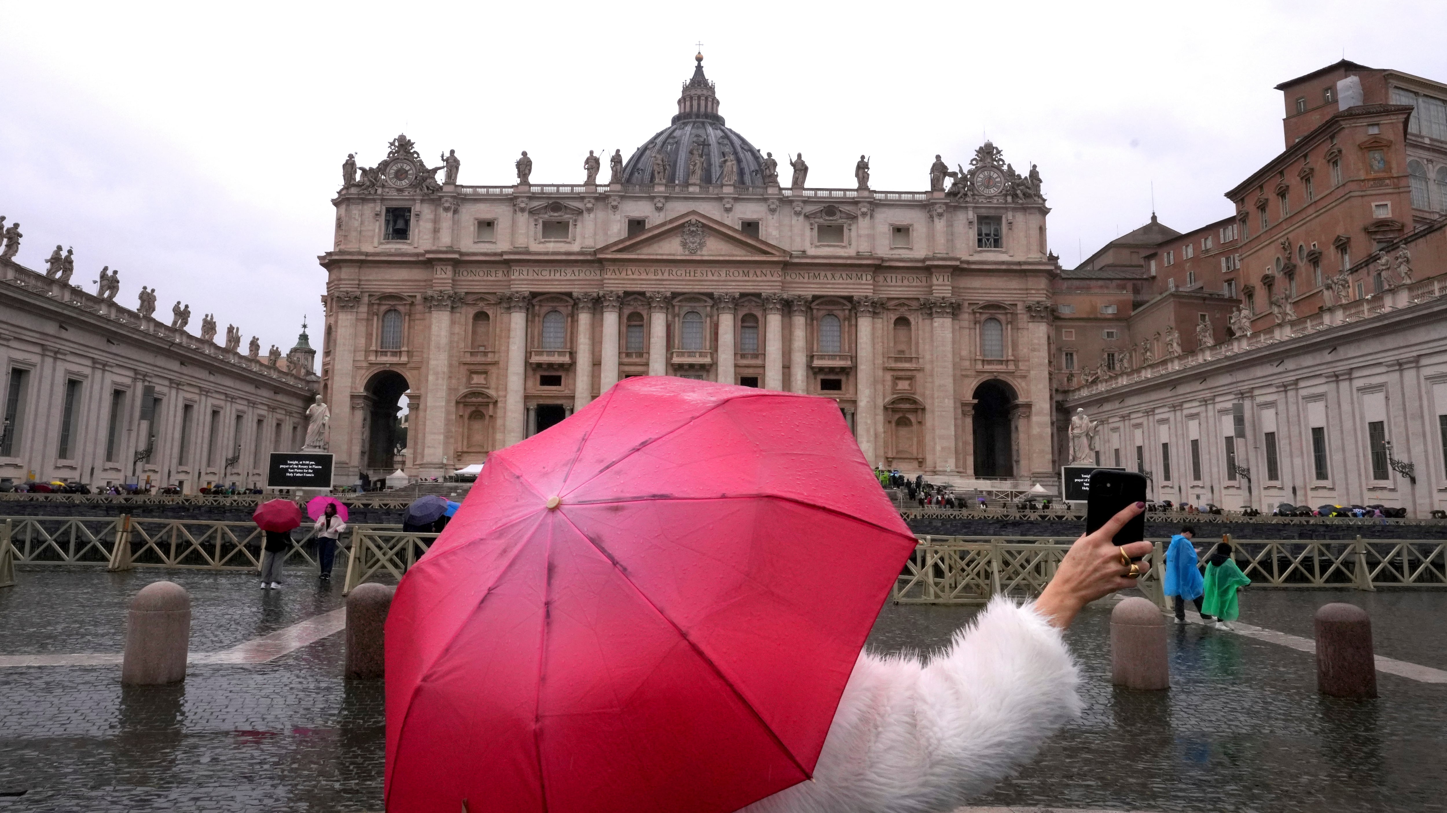 Una mujer toma fotos bajo la lluvia en la plaza de San Pedro en el Vaticano, el sábado 1 de marzo de 2025. (AP Foto/Kirsty Wigglesworth)
