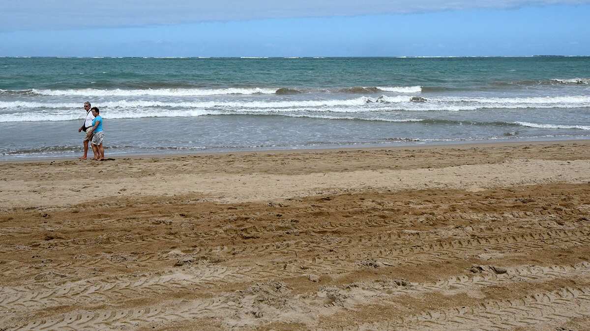 Una pareja camina a la distancia en una playa.