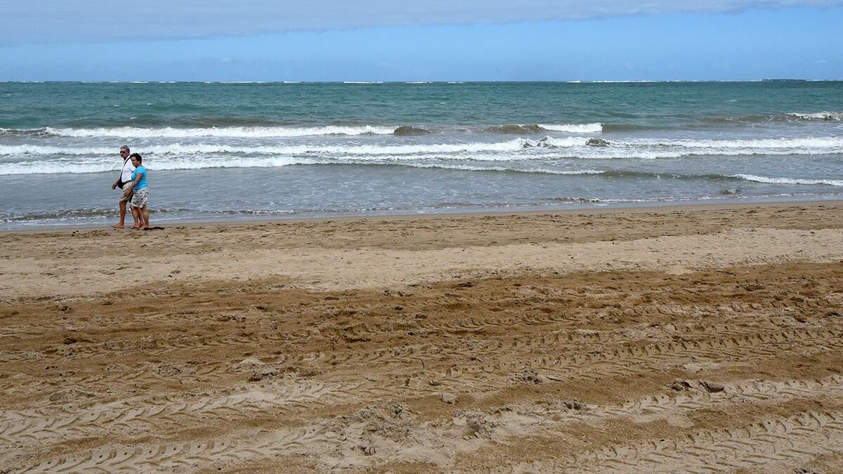 Una pareja camina a la distancia en una playa.