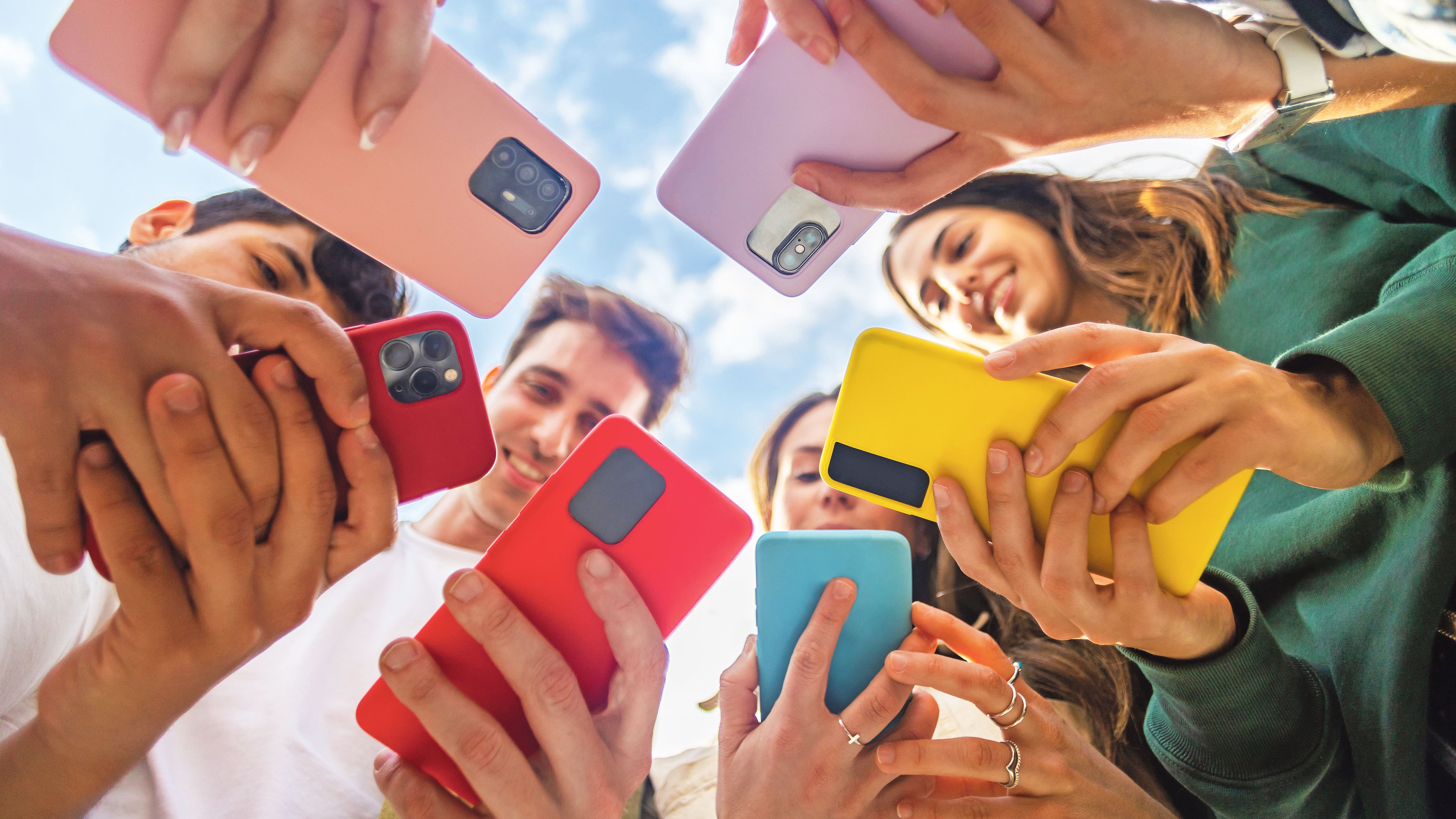 Grupo de jóvenes usando teléfonos móviles de pie en círculo al aire libre