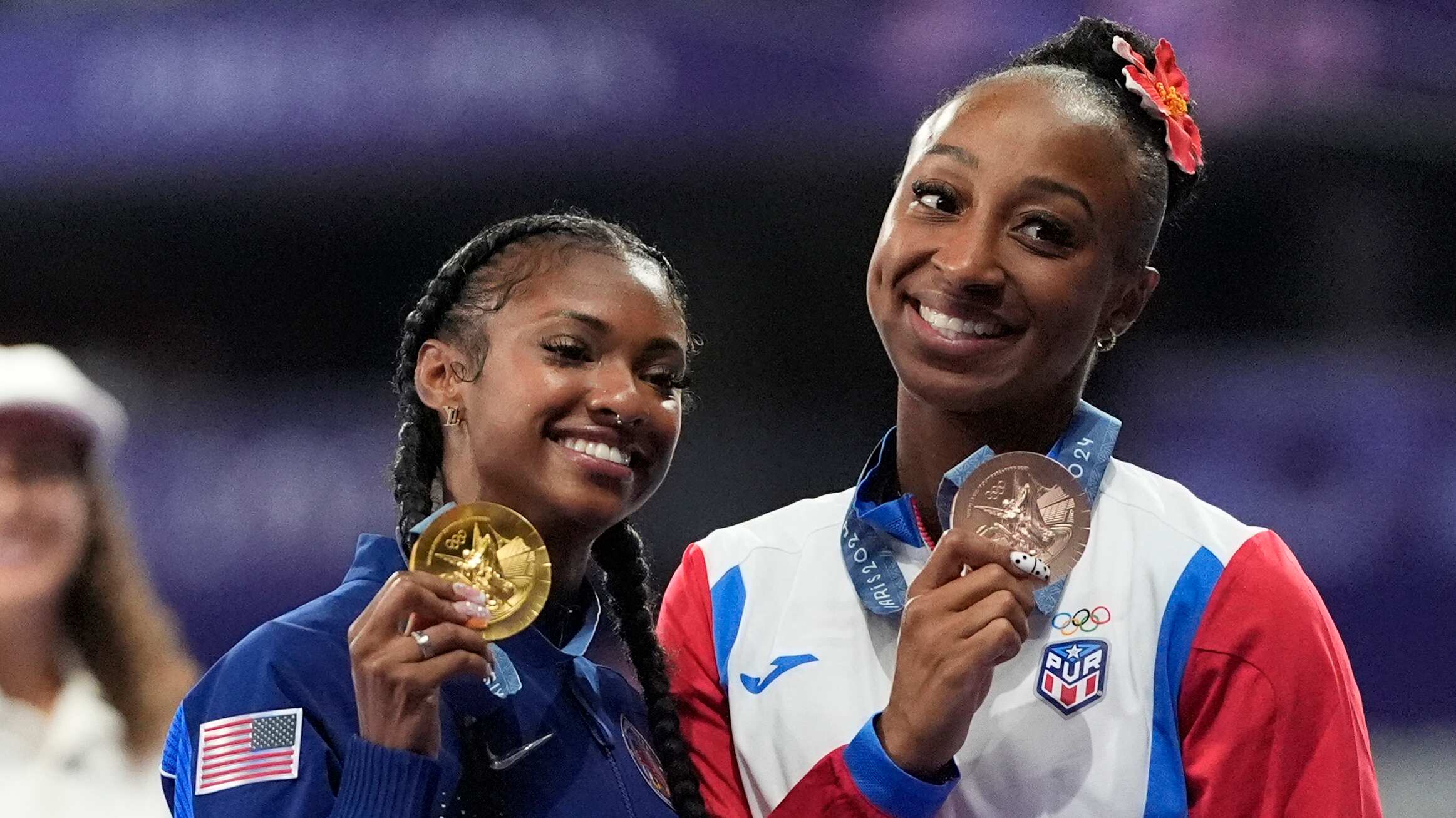 Masai Russell, medallista de oro en los 100 metros con vallas femeninos, en el centro, de Estados Unidos, y Jasmine Camacho-Quinn, medallista de bronce, de Puerto Rico, en el podio de los Juegos Olímpicos de Verano de 2024, el sábado 10 de agosto de 2024, en Saint-Denis, Francia. (Foto AP/Matthias Schrader)