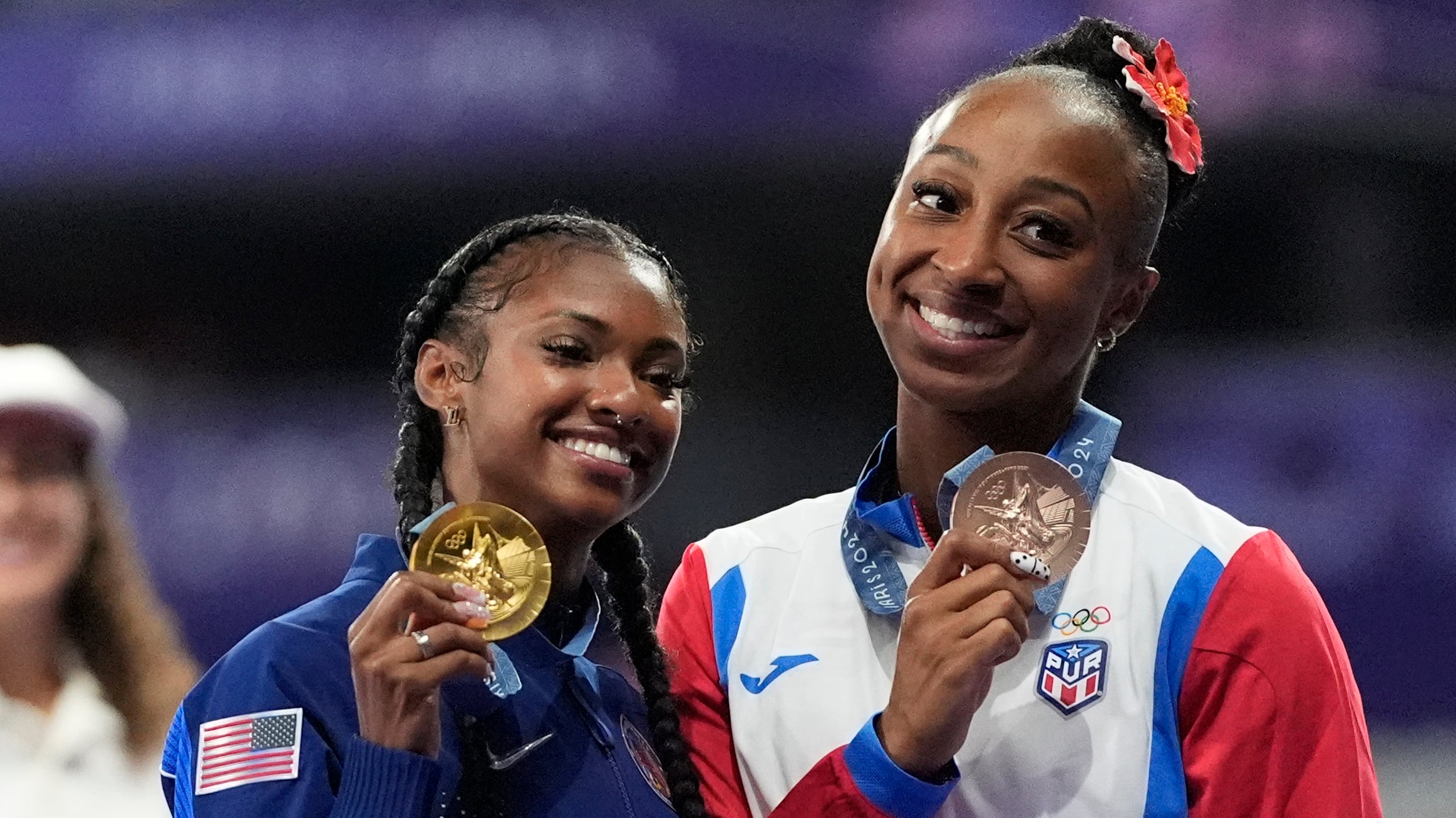 Masai Russell, medallista de oro en los 100 metros con vallas femeninos, en el centro, de Estados Unidos, y Jasmine Camacho-Quinn, medallista de bronce, de Puerto Rico, en el podio de los Juegos Olímpicos de Verano de 2024, el sábado 10 de agosto de 2024, en Saint-Denis, Francia. (Foto AP/Matthias Schrader)