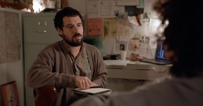 Juan Botta como el doctor Lorenzo Piovanetti frente a un escritorio y sujetando una libreta frente a Vei Habache.