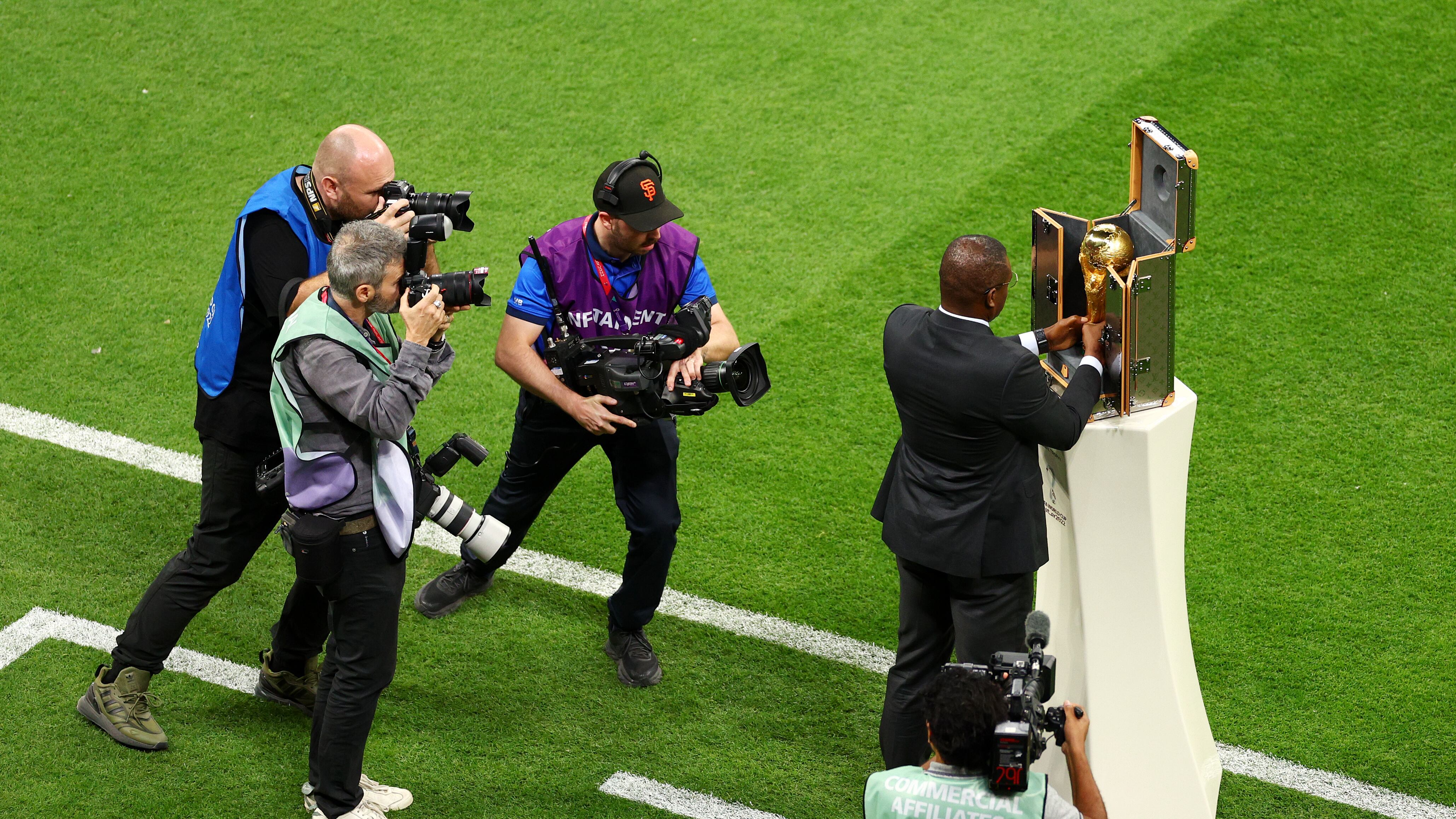 Marcel Desailly toca el trofeo de la Copa Mundial mientras fotoperiodistas y videógrafos se le acercan en el campo.