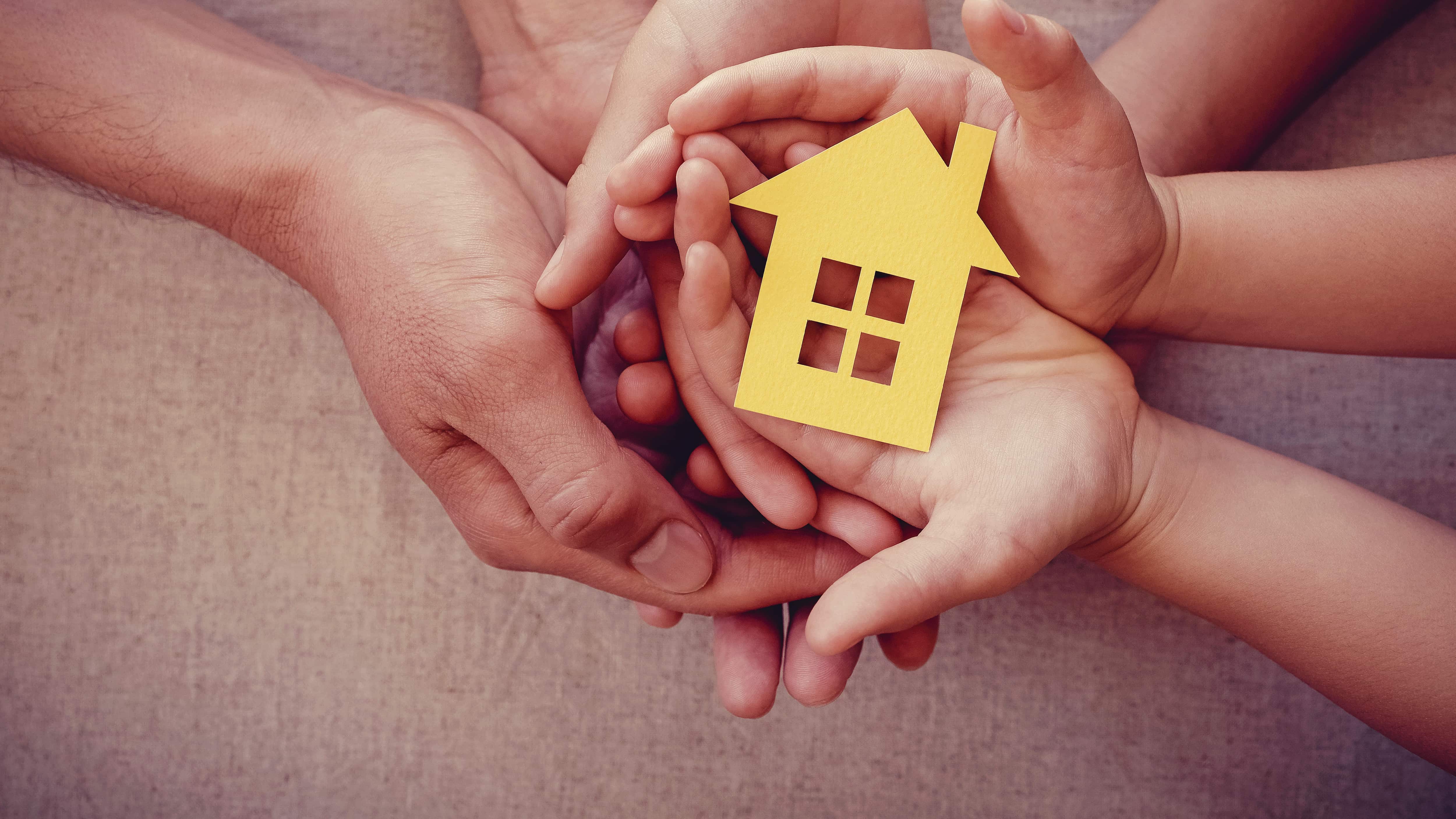 Manos de adultos y niños sosteniendo el concepto de casa amarilla, hogar familiar y refugio para personas sin hogar