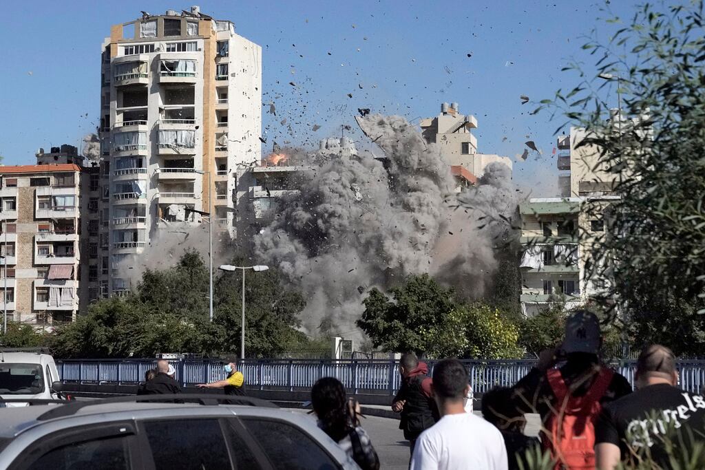 Varias personas observan el derrumbe de un edificio tras ser alcanzado por un ataque aéreo israelí en Ghobeiri, Beirut, Líbano, el martes 22 de octubre de 2024. (Foto AP/Bilal Hussein)