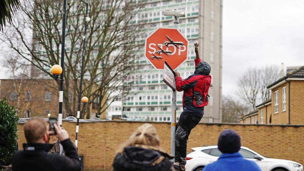 Una persona retira una obra de arte de Banksy que parece mostrar tres drones sobre un cartel de Stop que fue develado en la intersección de las calles Southampton Way y Commercial Way en Peckham, sureste de Londres, viernes 22 de diciembre de 2023. (Aaron Chown/PA via AP)