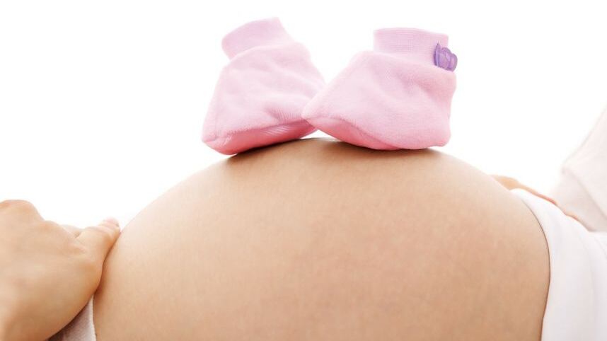 La panza de una mujer recostada, sobre la que descansan botines rosados de bebé.