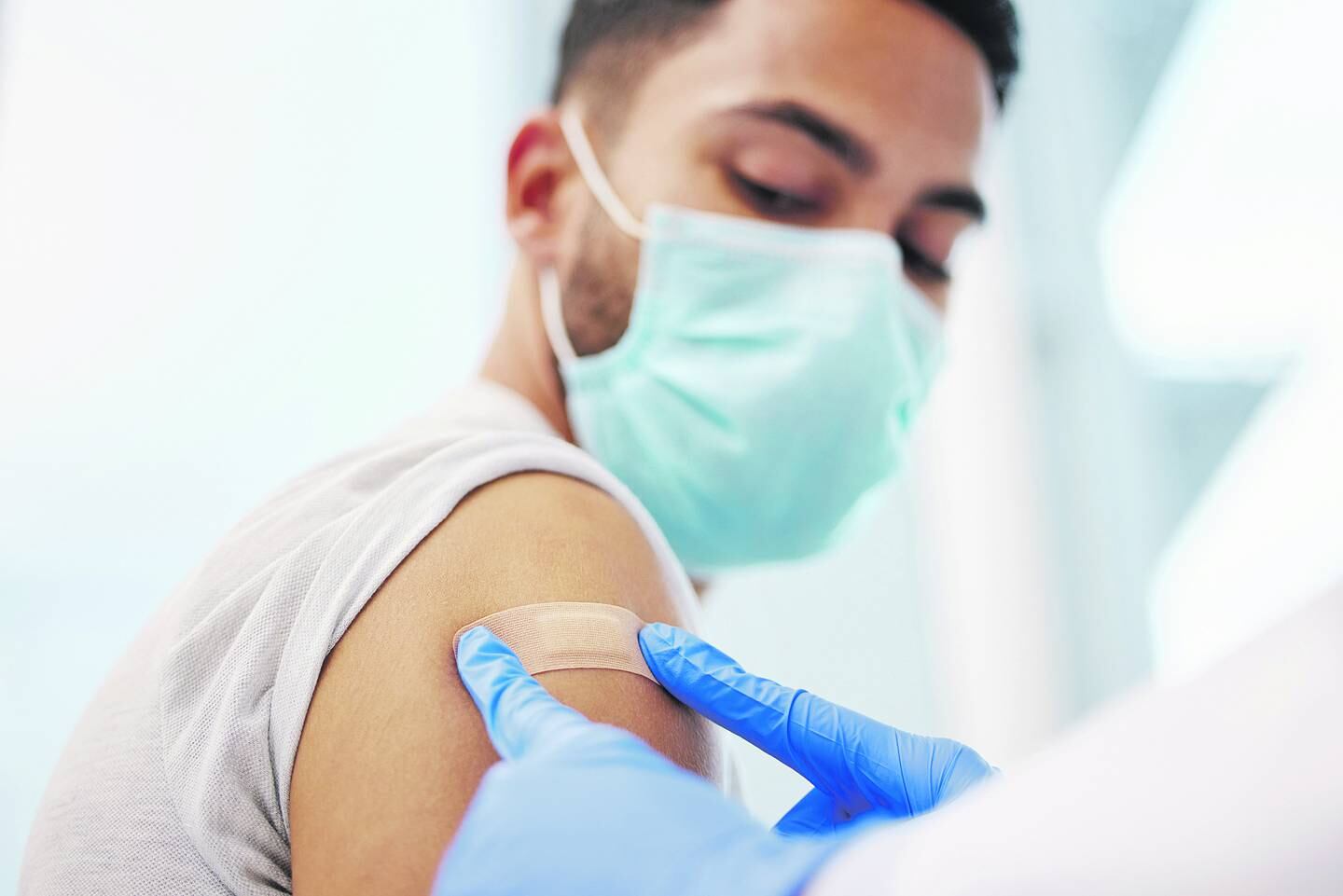 Le colocan una curita a un joven en el brazo después de ponerle una vacuna.